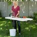 A woman washing vegetables on a white Lifetime plastic folding table outdoors.