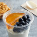 A Fabri-Kal divided clear PET parfait cup with yogurt, blueberries, and honey on a table.
