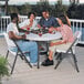 A group of people sitting around a Lifetime white granite plastic folding table with drinks.