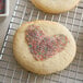 A heart-shaped cookie with Rainbow Sanding Sugar sprinkles on top.