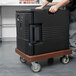 A man pushing a black Cambro Camdolly with a dark brown container on it.