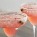 Two pink drinks with ice and strawberries on top in a glass of pink salt.