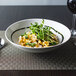 A white porcelain bowl filled with pasta with a glass of wine.
