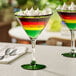 Two Acopa Tropic martini glasses with green rims and bases filled with multicolored drinks.
