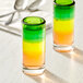 A close-up of two Acopa Tropic shooter glasses with green, yellow, and red liquid.