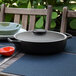 A black Front of the House stoneware ovenware dish with a lid on a table with a bowl and a pot.