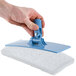 A hand holding a blue and white Scrubble by ACS light-duty scouring pad.