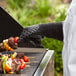 A person wearing Outset oven gloves cooking food on a grill.