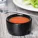 A Tuxton black china ramekin filled with red sauce on a table.