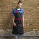 A woman wearing a black Uncommon Chef Rebel Bib Apron with red webbing.