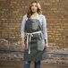 A woman wearing a Uncommon Chef pinstripe denim apron with natural webbing.