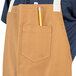 A man wearing a brown Uncommon Chef Rebel bib apron with natural webbing and 3 pockets, with a pencil in one pocket.