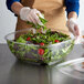 A woman in gloves preparing a salad in a Fineline clear plastic bowl.
