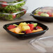 A black Fineline plastic bowl filled with fruit salad on a counter.