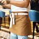A person wearing a brown Uncommon Chef waist apron with natural webbing and 3 pockets.