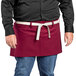 A man in a black shirt wearing a red Uncommon Chef waist apron with natural webbing.