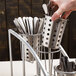 A hand taking metal utensils from a Cal-Mil vertical steel holder.