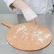 A person wearing white gloves and putting flour on a pizza board.