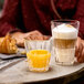 A woman holding a Spiegelau Perfect Serve tumbler of orange juice and a glass of coffee on a table with a croissant.