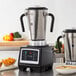 An AvaMix commercial food blender with a black handle sits on a counter next to bowls of soup and cut up pumpkin.