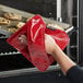 A hand using a red and black San Jamar EZ-KLEEN® hot pad to hold a tray of cookies.