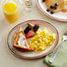 A plate of scrambled eggs, a breakfast sandwich, and fruit on an Acopa brown speckle narrow rim oval platter.