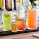 A row of Acopa Madras Rocks glasses filled with different colored drinks on a cocktail bar.