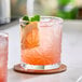 A pink beverage with ice, a lemon slice, and mint leaves served in an 11 oz. patterned rocks glass on a coaster.