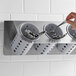 A Steril-Sil stainless steel flatware organizer with gray plastic cylinders holding a spoon and fork.