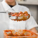 A chef uses a Vollrath Orange Perforated Oval Spoodle to serve meatballs.