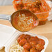 A Vollrath orange perforated oval spoon with a hole in the middle of the bowl scooping out spaghetti and meatballs.