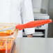 A person in a white coat using a Vollrath orange perforated oval Spoodle over a glass bowl of red sauce.