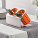 A Steril-Sil stainless steel flatware holder with orange perforated plastic cylinders holding silverware.