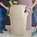 A couple of people standing next to a Continental beige square trash can with two doors.