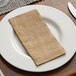 A white plate with a Hoffmaster burlap print dinner napkin on it.