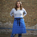 A woman wearing a blue Uncommon Chef mod waist apron.