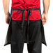 A person wearing a red waist apron with black trim.