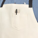 An ivory Uncommon Chef bib apron with black webbing and 3 pockets.
