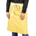 A woman wearing a yellow Uncommon Chef waist apron with white webbing.