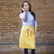 A woman standing on a kitchen counter wearing a yellow Uncommon Chef waist apron with 3 pockets.