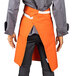 A man wearing an orange Uncommon Chef waist apron with natural webbing and 3 pockets.