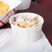 A Solo white paper souffle cup filled with coleslaw on a counter.