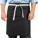 A man wearing a black Uncommon Chef waist apron with white straps.