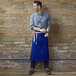 A man wearing a Uncommon Chef royal blue canvas apron with natural webbing and a pocket.