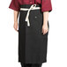 A woman wearing a black Uncommon Chef Marvel Bistro apron with natural webbing.