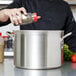 A hand pours seasoning into a Vollrath stainless steel sauce pot.