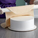 A person rolling out dough on a round white Baker's Mark cake dummy.