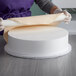 A woman in purple gloves wrapping a Baker's Mark foam round cake dummy in paper.