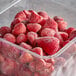 A plastic container full of red organic whole strawberries.