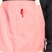 A person wearing a coral pink Uncommon Chef canvas bib apron with natural webbing and 3 pockets.